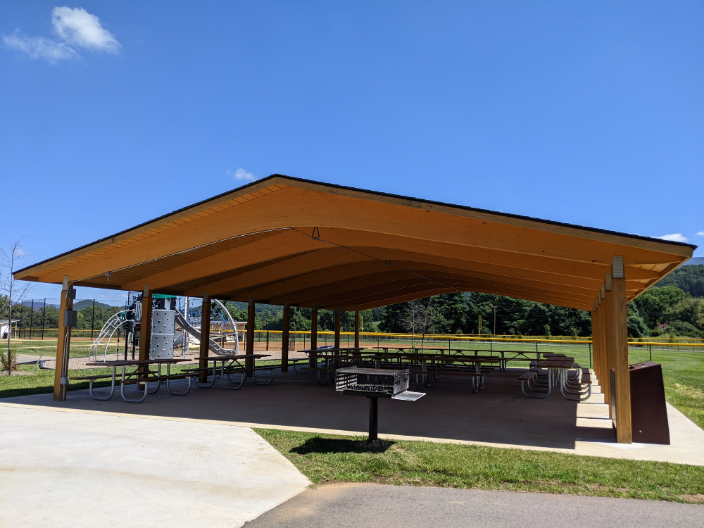 The shelter at Creed Fields Park is shown next to the playground and baseball field on a sunny summer day.