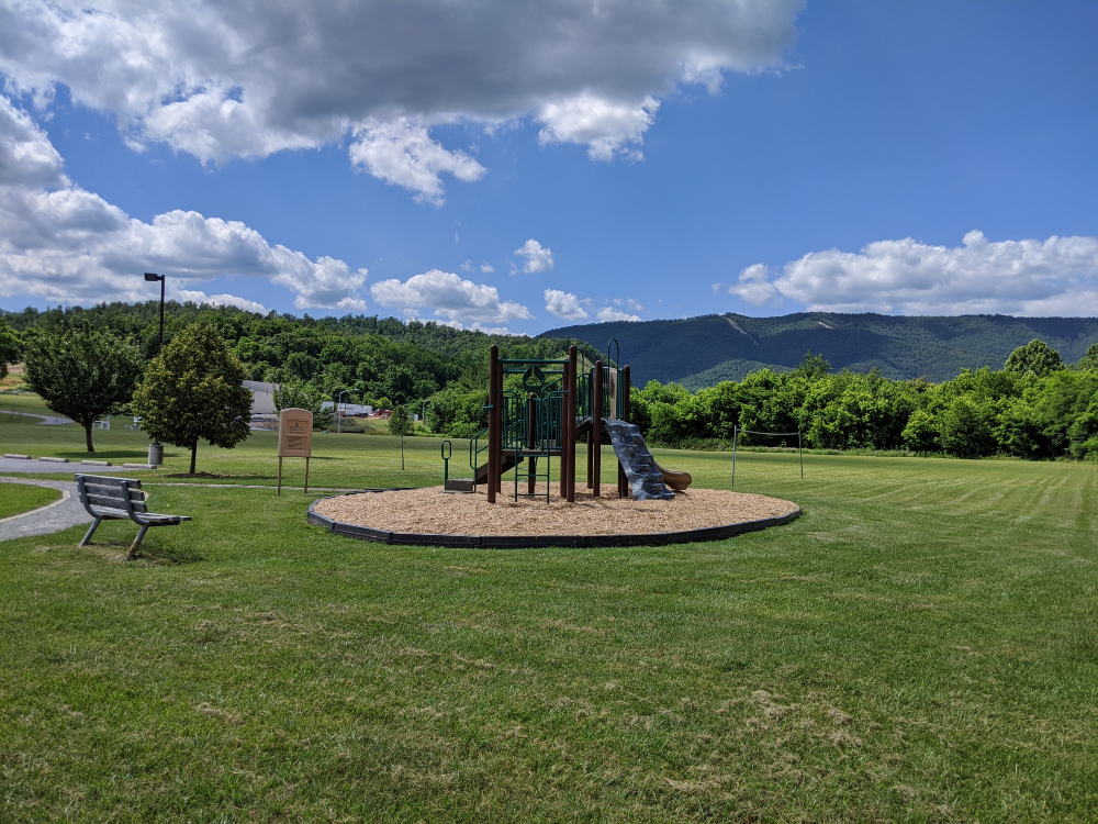A view of the playground and open green space at Eastern Montgomery Park with a mountain backdrop on a sunny summer day.