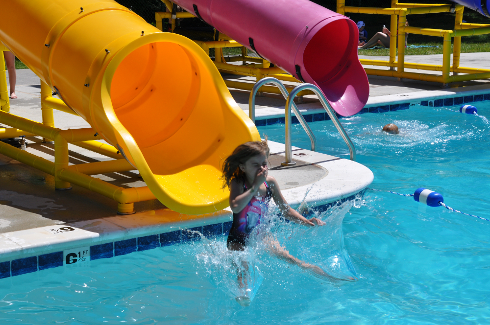 A child goes down the big slide and makes a splash at the Frog Pond Pool on a sunny summer day.