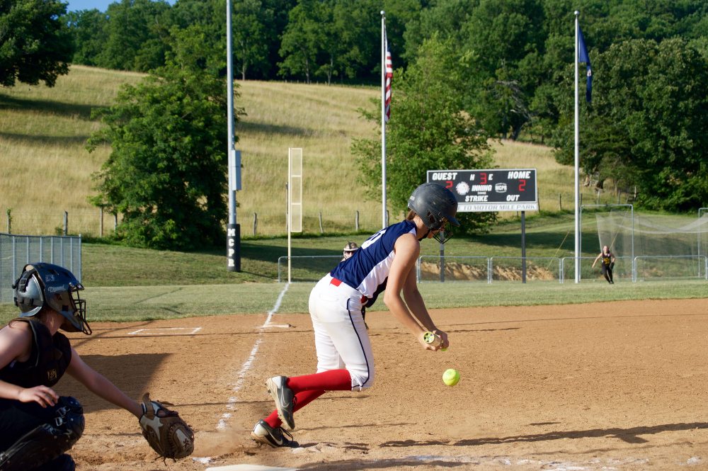 A softball player bunts the ball in front of home plate and begins her run towards first base.